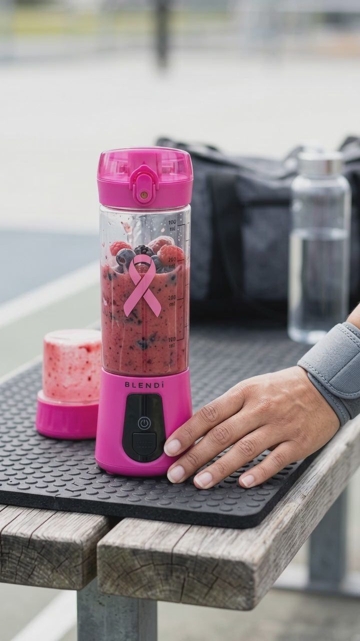 Hot Pink BLENDi Pro+ Breast Cancer Awareness Edition blending a berry smoothie on a gym bench